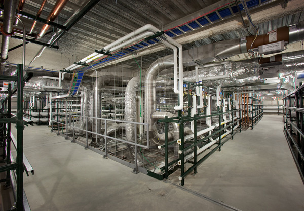 Interior of a large industrial facility showing extensive overhead piping and mechanical infrastructure