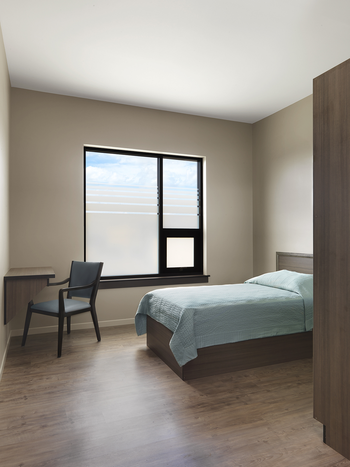 clean modern resident room with bed, desk, and window