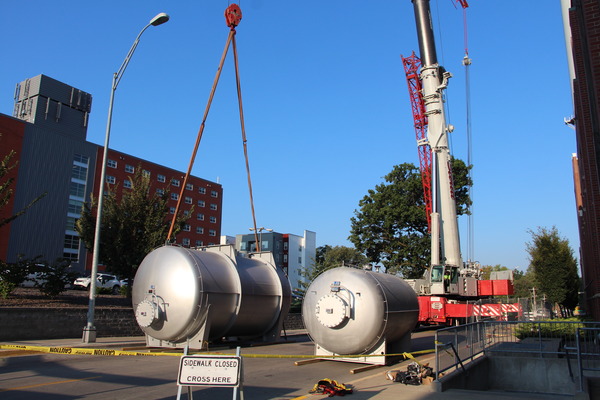 crane lifting large power plant tanks from street