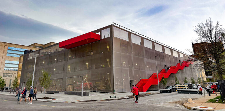 Modern multi-story building exterior with red accent panels under blue sky