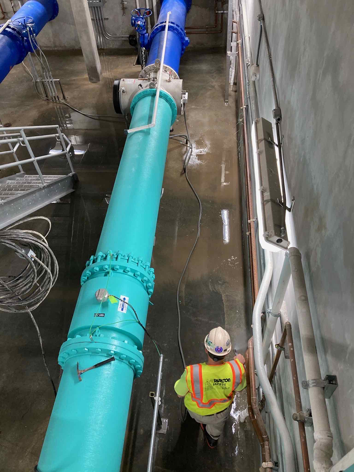Worker in safety gear inspecting blue utility pipes at a construction site