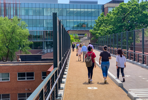 People walking along an outdoor pedestrian walkway adjacent to a brick building